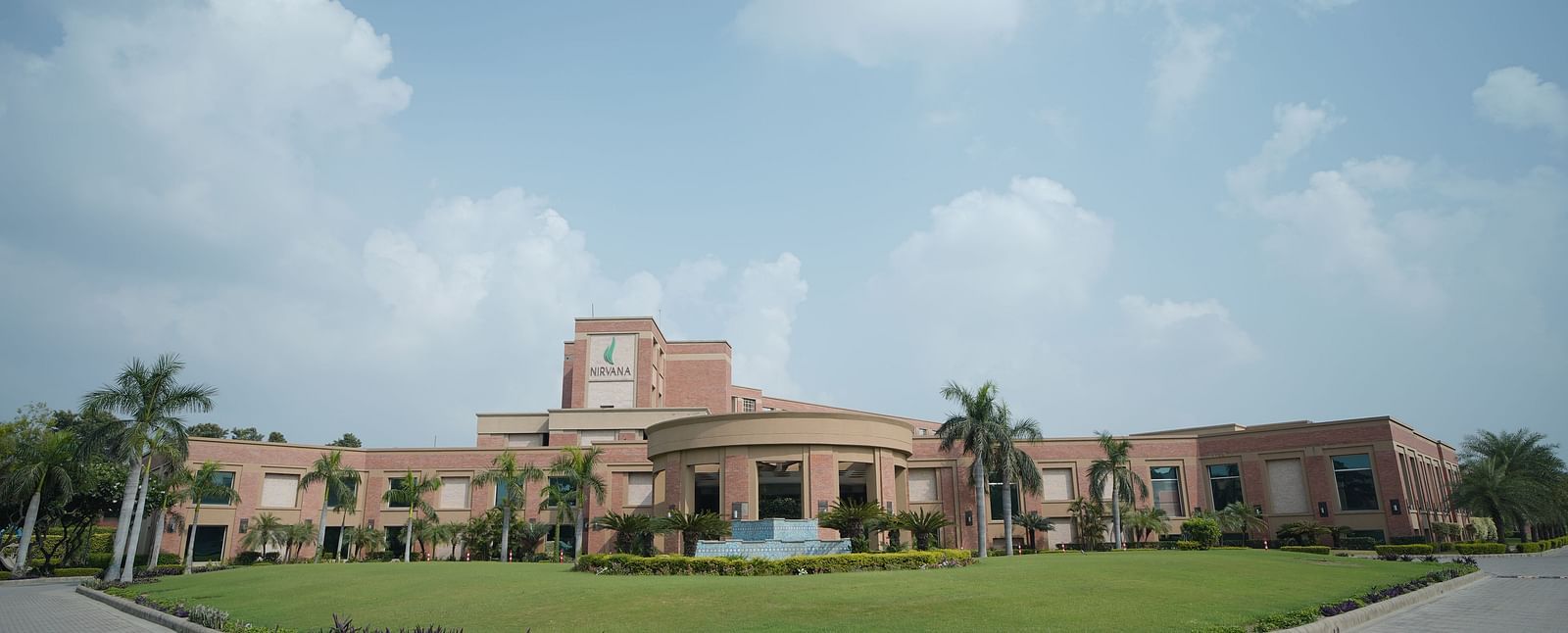 Exterior panoramic view of Nirvana Luxury Hotel, Ludhiana during the day with a pathway and a manicured garden in view.