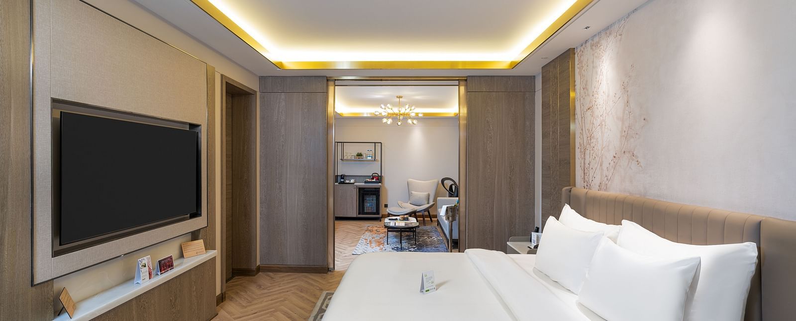 Nirvana Suite bedroom featuring a bed, wall-mounted TV, subtle ambient lighting, and a glimpse into the suite layout - Nirvana Luxury Hotel, Ludhiana