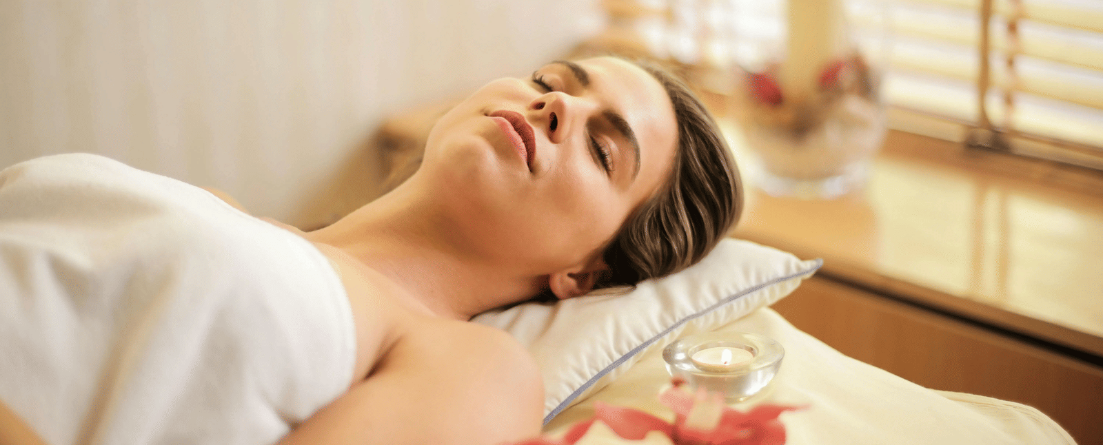 A woman lying down on a bed all relaxed in a brightly lit room.
