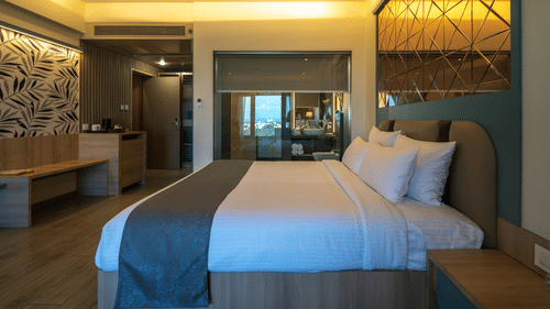 A hotel room featuring a double bed with grey and white bedding, reflective surfaces, and warm ambient lighting | Pride Elite Chhatrapati Sambhajinagar