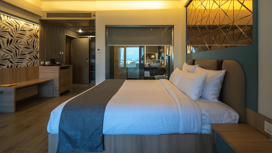 A hotel room featuring a double bed with grey and white bedding, reflective surfaces, and warm ambient lighting | Pride Elite Chhatrapati Sambhajinagar