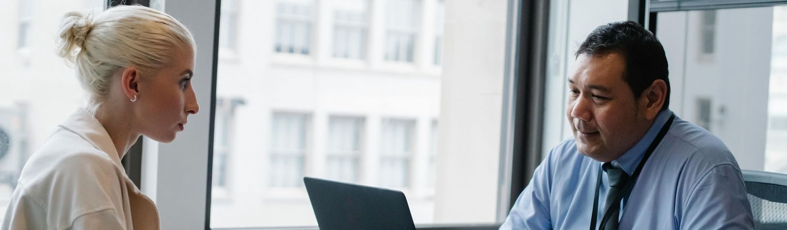 Two professionals are engaged in a discussion at an office desk with a laptop. 