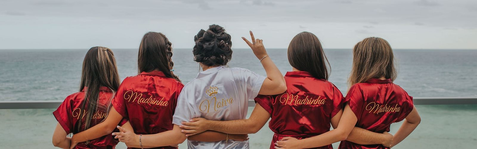a bride and bridesmaids holding each other and looking into the sea with cloud cover - Bachelorette in Bangkok