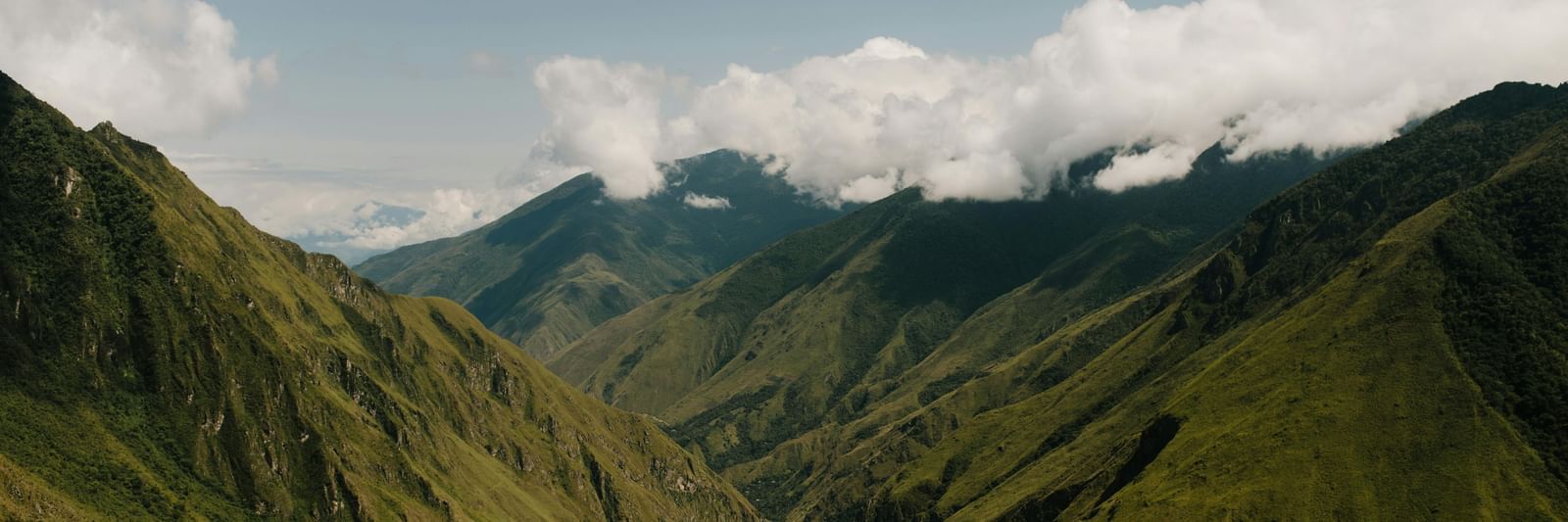 A verdant green mountains with deep valleys and misty clouds in the distance.
