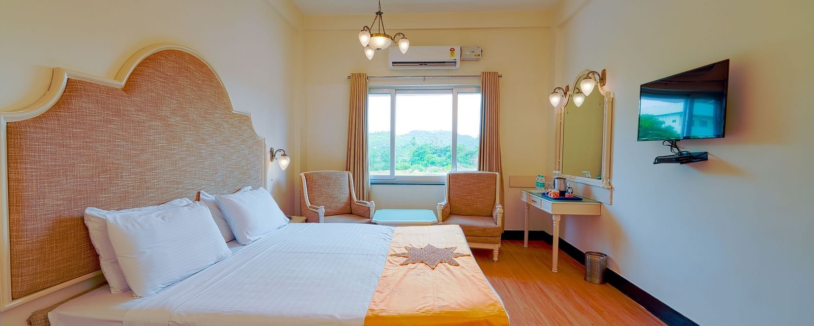 A well-appointed hotel room with a large bed, orange throw, wooden flooring, and a TV. - Greens Inn - Cozy Accommodations