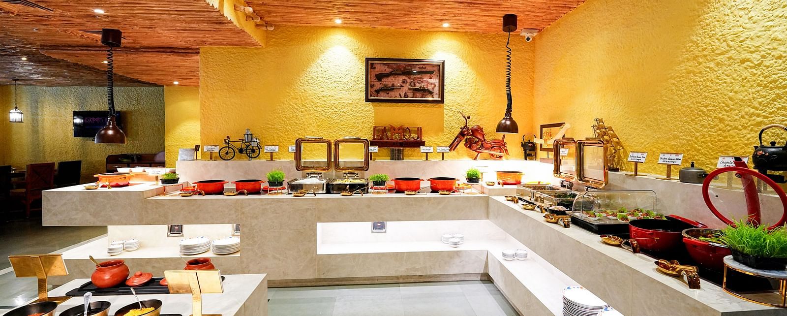 A comprehensive view of a buffet setup in a room with a rustic ceiling and yellow walls. - Tara, Comfort Hotel in Hyderabad - Ramoji Film City.