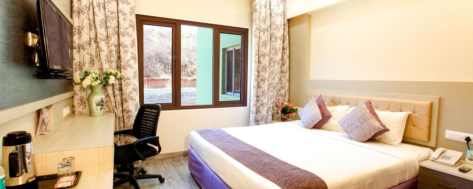 A modern hotel room with a plush king-sized bed and a view of the outdoors. - Tara, Comfort Hotel in Hyderabad - Ramoji Film City.
