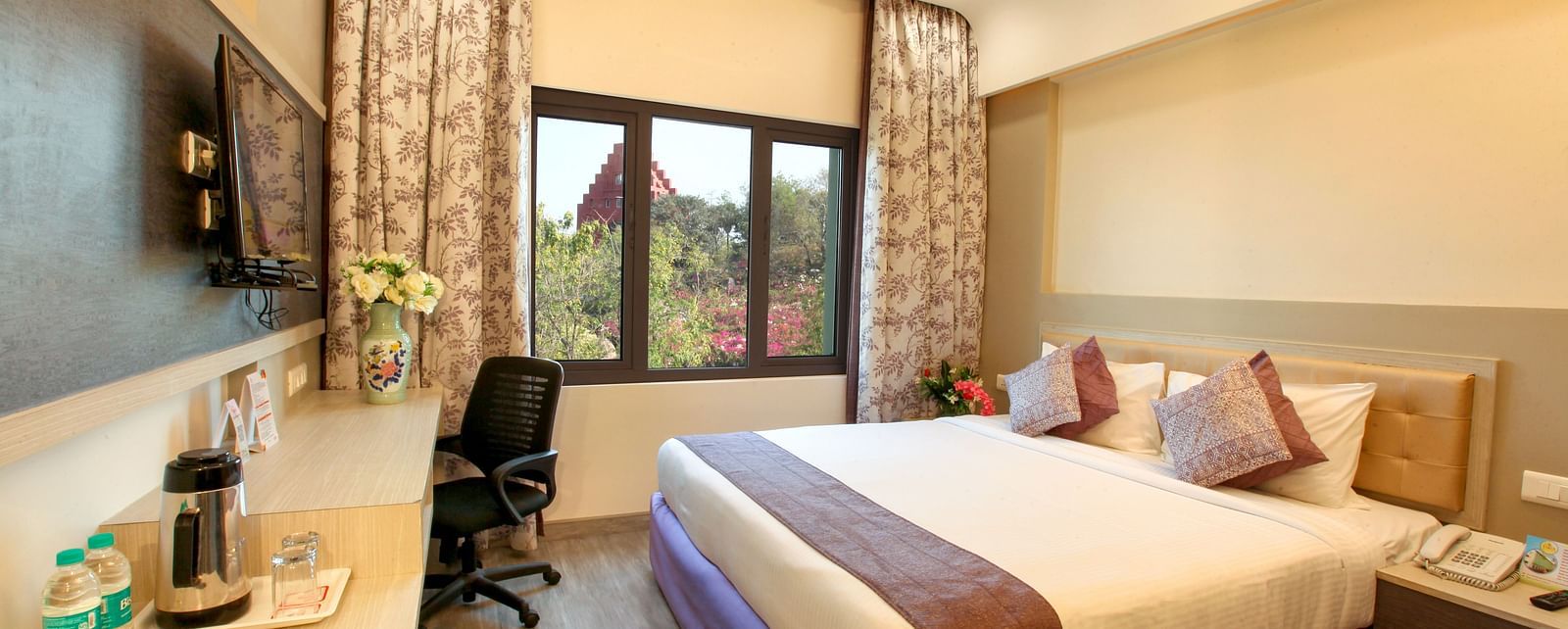A spacious and elegantly decorated hotel room with a large window and a work area. - Tara, Comfort Hotel in Hyderabad - Ramoji Film City.