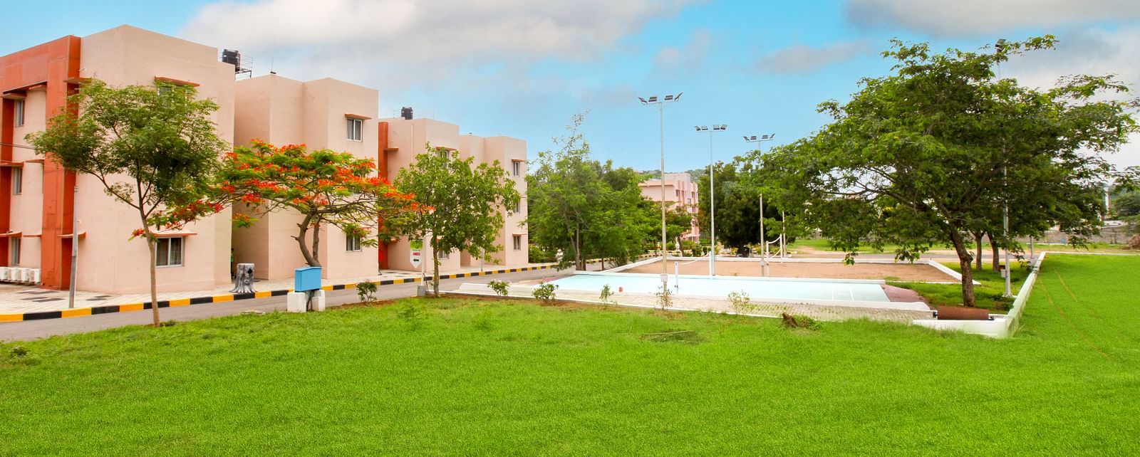 A vibrant exterior shot of a pink hotel building with greenery and a red security booth in the foreground at Sahara - Quality Accommodations in Ramoji Film City, Hyderabad.