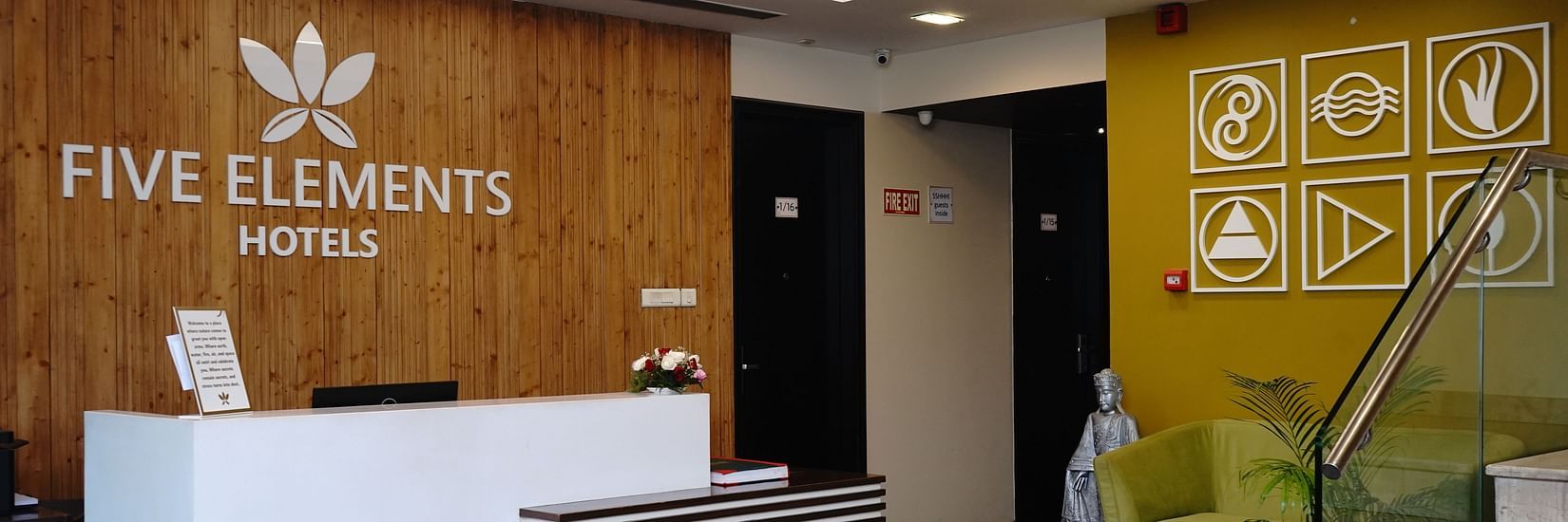 An image of a reception lobby at Five Elements Hotels North Avenue, Delhi featuring a reception desk, a sofa, and a staircase next to it