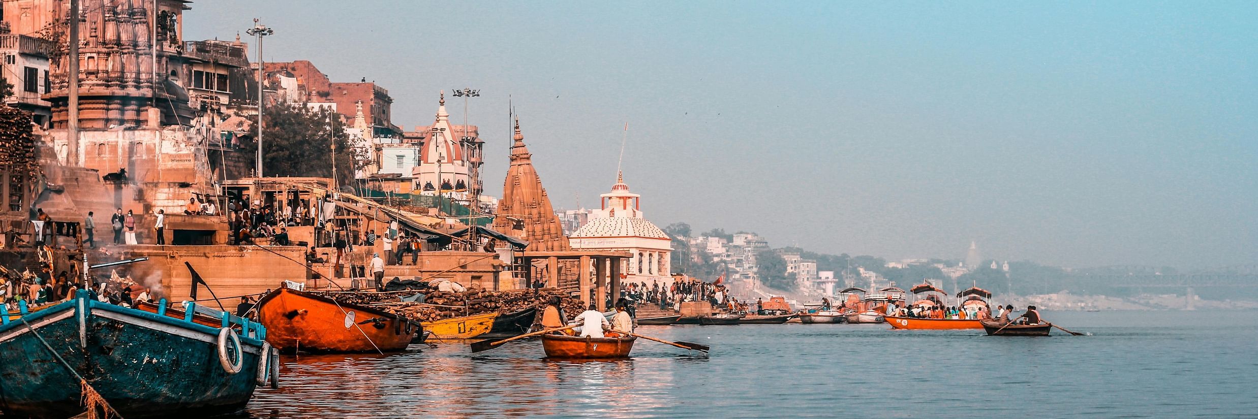 A bright morning scene showcasing the ghats, boats, and historic architecture.