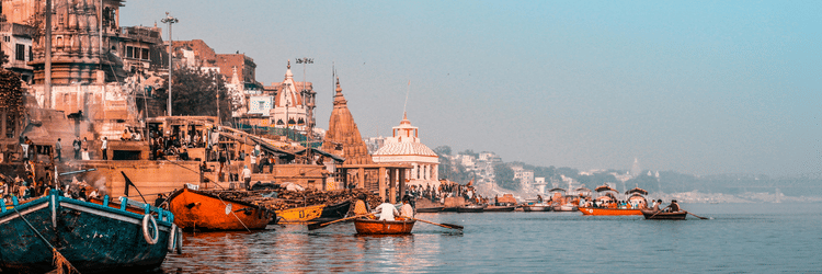 A bright morning scene showcasing the ghats, boats, and historic architecture.