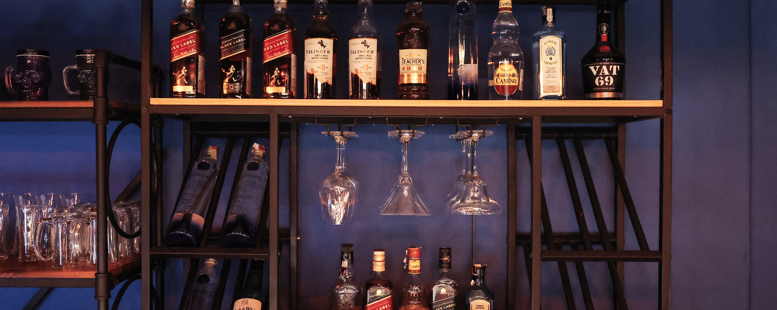 Close-up of the industrial-style black metal bar shelving with bottles of wine, spirits, and hanging glassware at Hotel Hukam's Lalit Mahal.