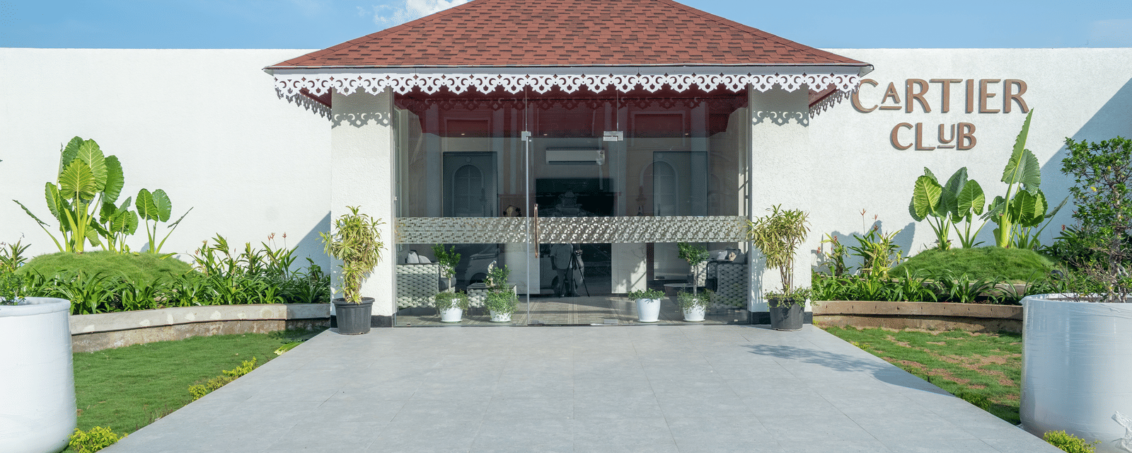 Exterior of the 'Cartier Club' building, a white structure with a red roof, fronted by a paved walkway and green lawn at Hotel Hukam's Lalit Mahal.