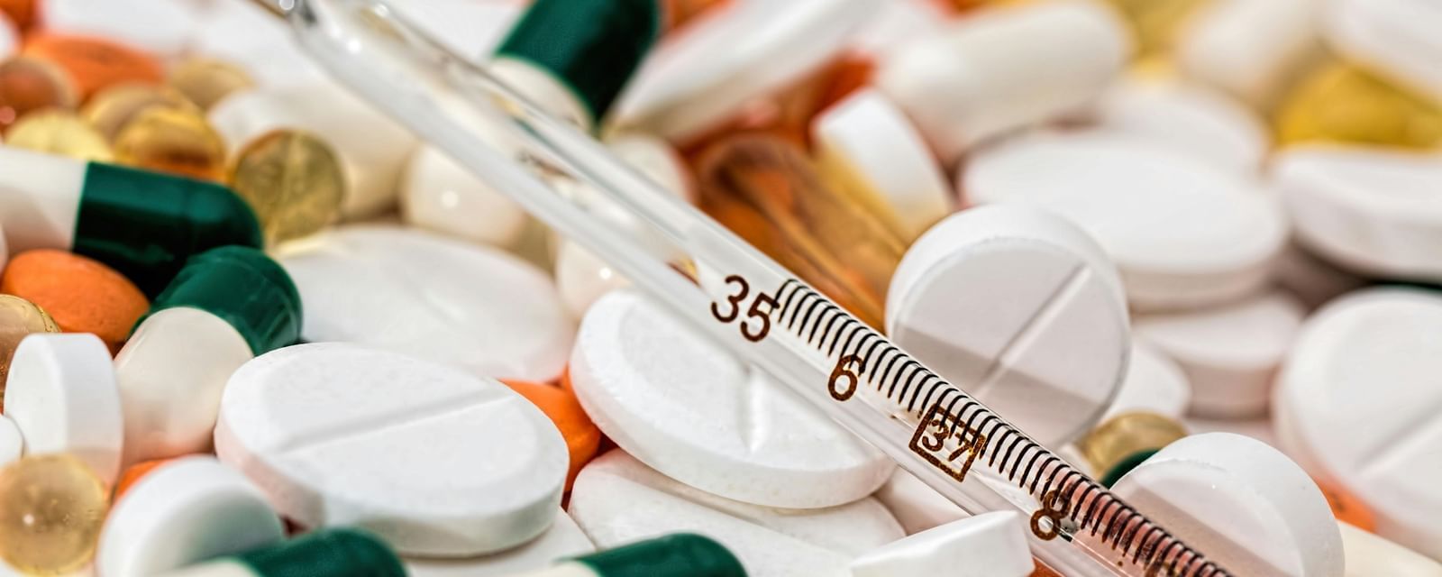 A collection of tablets and capsules with a thermometer.