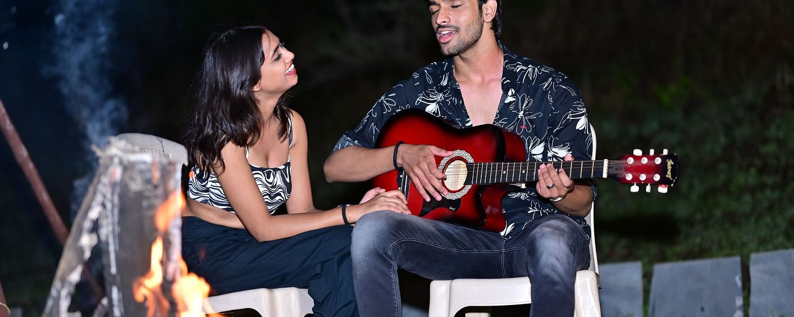 Couple playing guitar by a campfire at a camping site | Diamond Parks, Pune