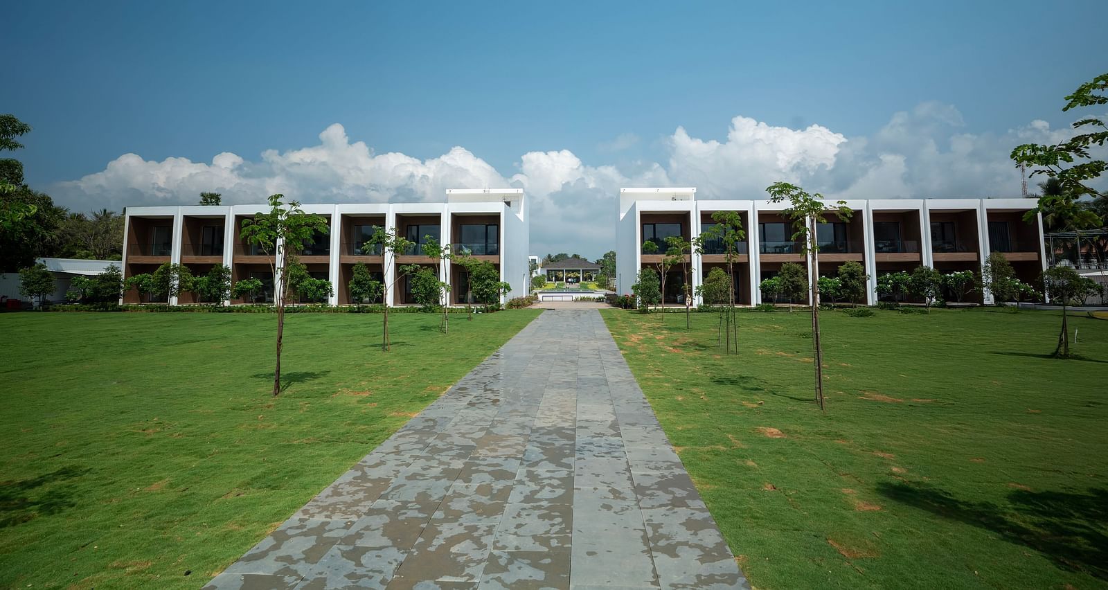  A lush green lawn at The Shore Trishvam, Pondicherry divided by a pathway in the middle with a clear blue sky in the background.