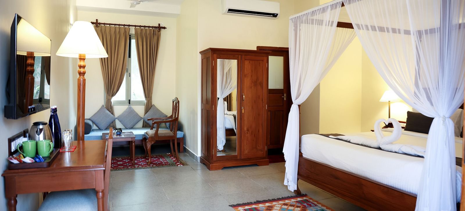A room that has a poster-bed, a cupoard, sitting area, table and chair, etc.A sitting area, a cupboard, and a tall lamp | Mango Hill La Serene, Pondicherry