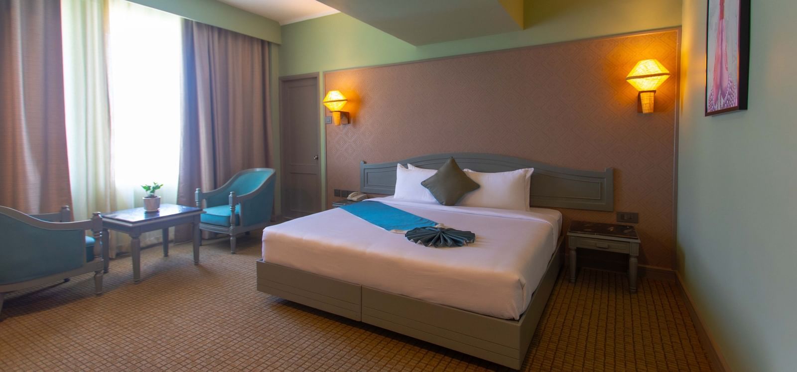 A hotel room at Shilton International, Kochi, with a large bed, a comfortable seating area, and large windows.