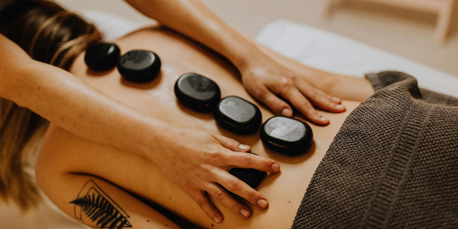A therapist performing a hot stone massage on a patient's back, gently placing the heated stones along the spine.