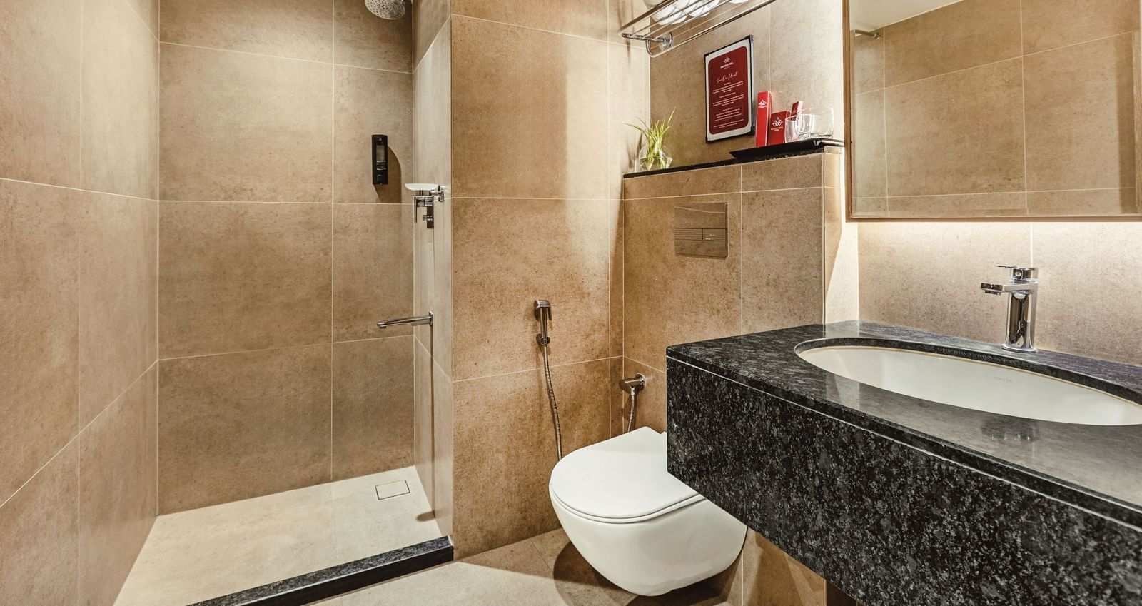 A wide view of the bathroom at Mango Hill Central, Chennai, showing the toilet, sink with a black counter, and a shower area.