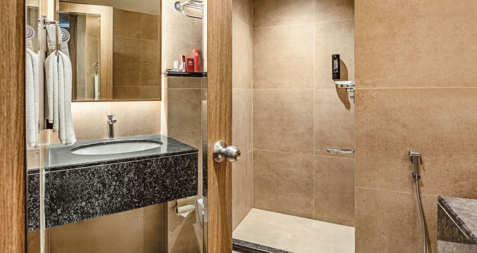 A view of the sink, mirror, and shower area in a bathroom at Mango Hill Central, Chennai. The walls are tiled in a beige colour.