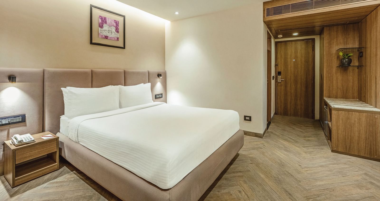 A wide-angle view of a room with a large bed at Mango Hill Central, Chennai. The room has a wooden wall feature.