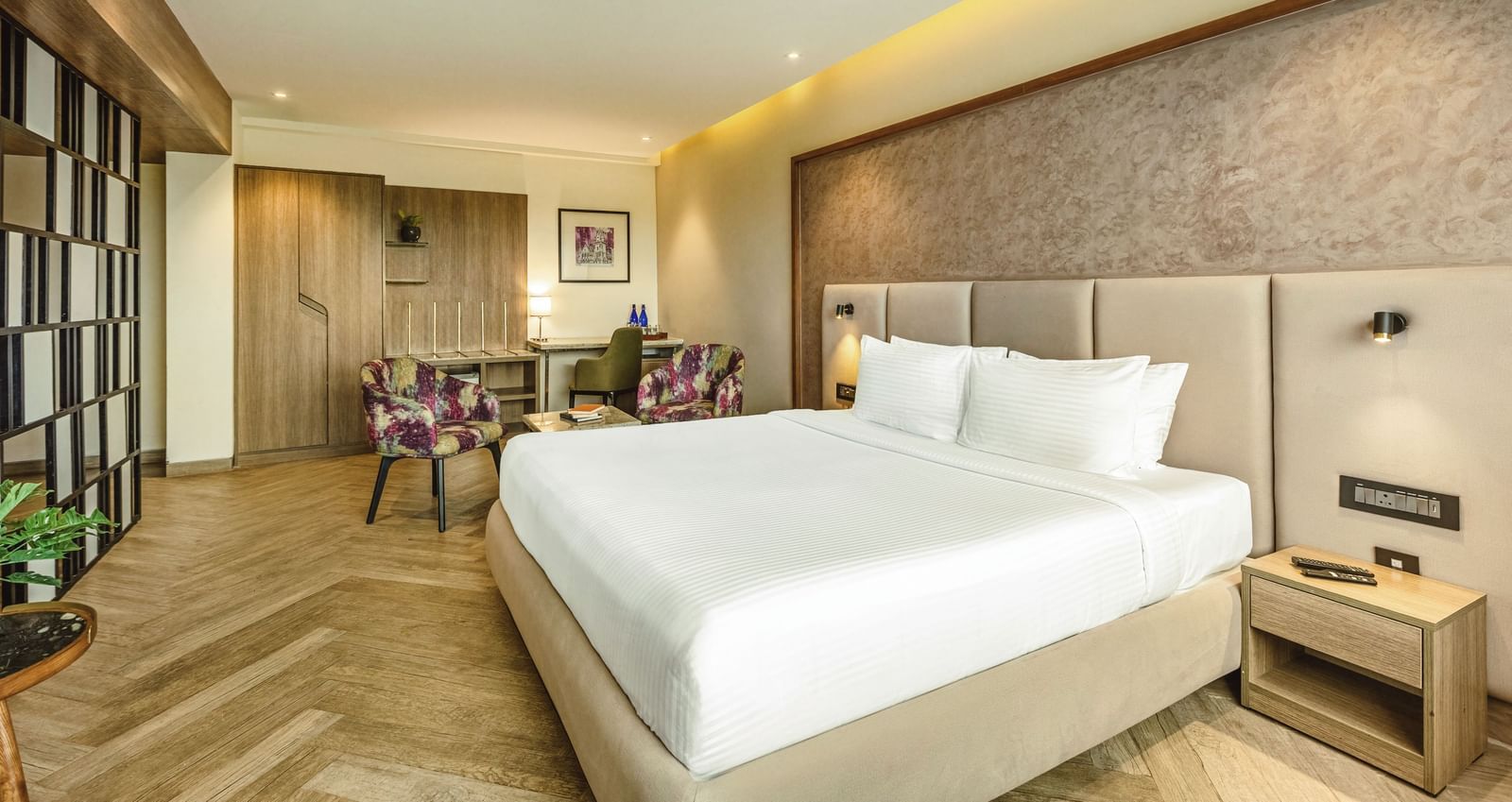 A wide-angle view of a room with a large bed at Mango Hill Central, Chennai. A desk and a chair are visible on the left.
