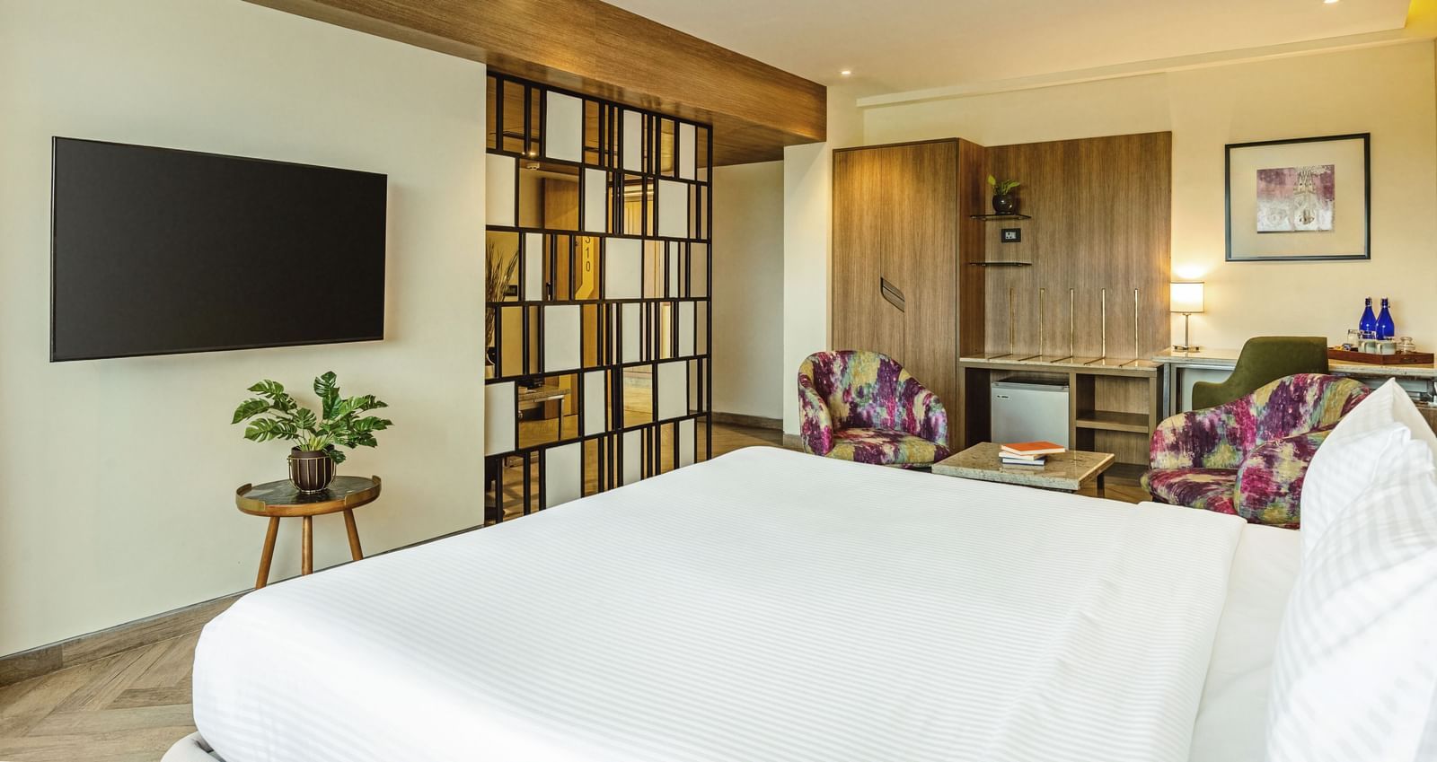  A wide-angle view of a room with a large bed and a television at Mango Hill Central, Chennai. A desk and chair are on the left.