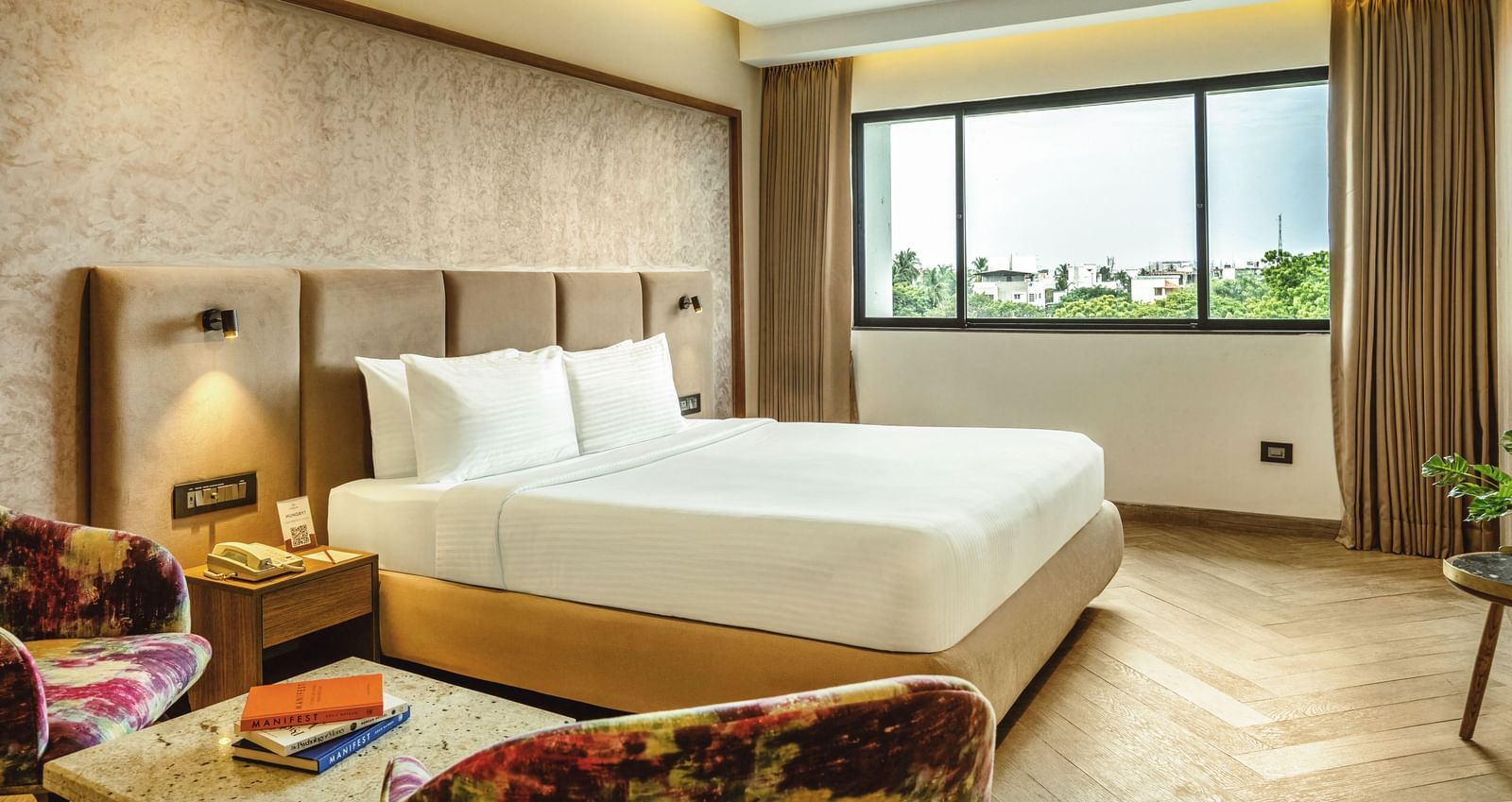 A wide-angle view of a room with a large bed at Mango Hill Central, Chennai. There is a large window on the far wall.