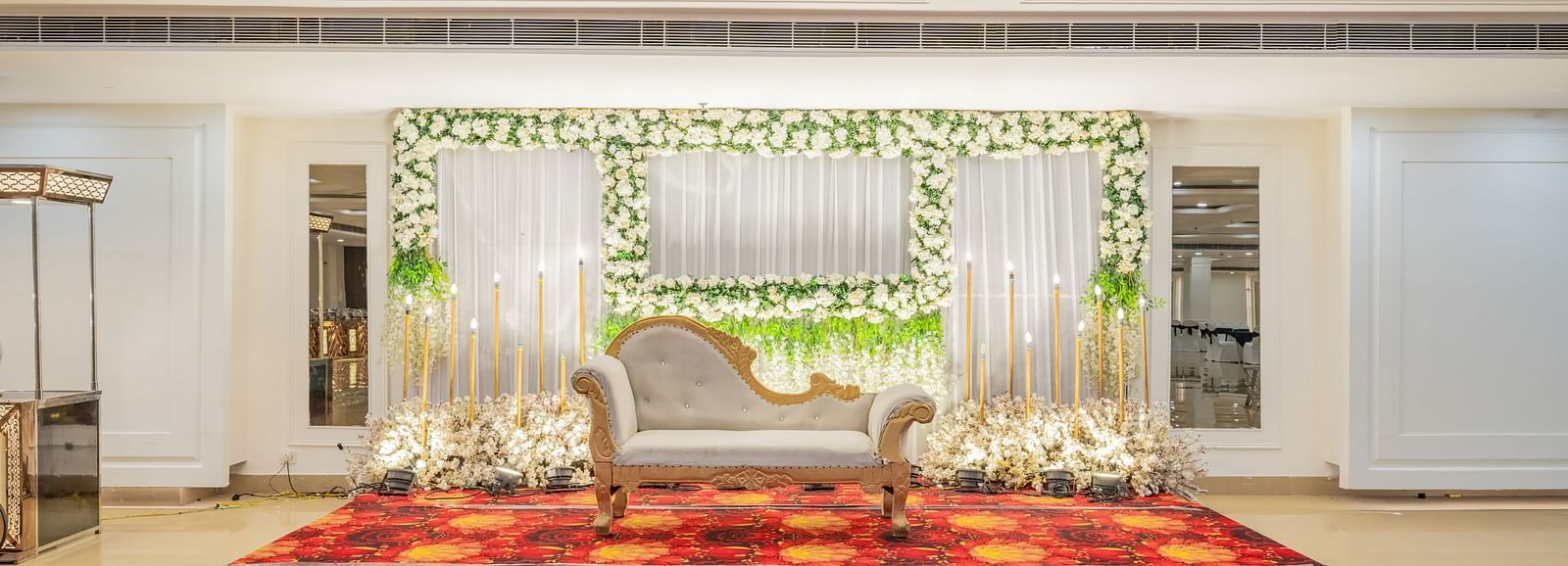 Indoor wedding stage setup with floral arrangements and red carpet at Hotel Highway King, Bilaspur.