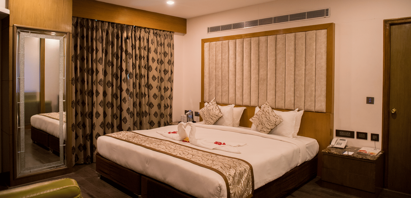 A hotel room at Benzz Park Chennai featuring a neatly made bed with white linens, a bedside table, and curtains.