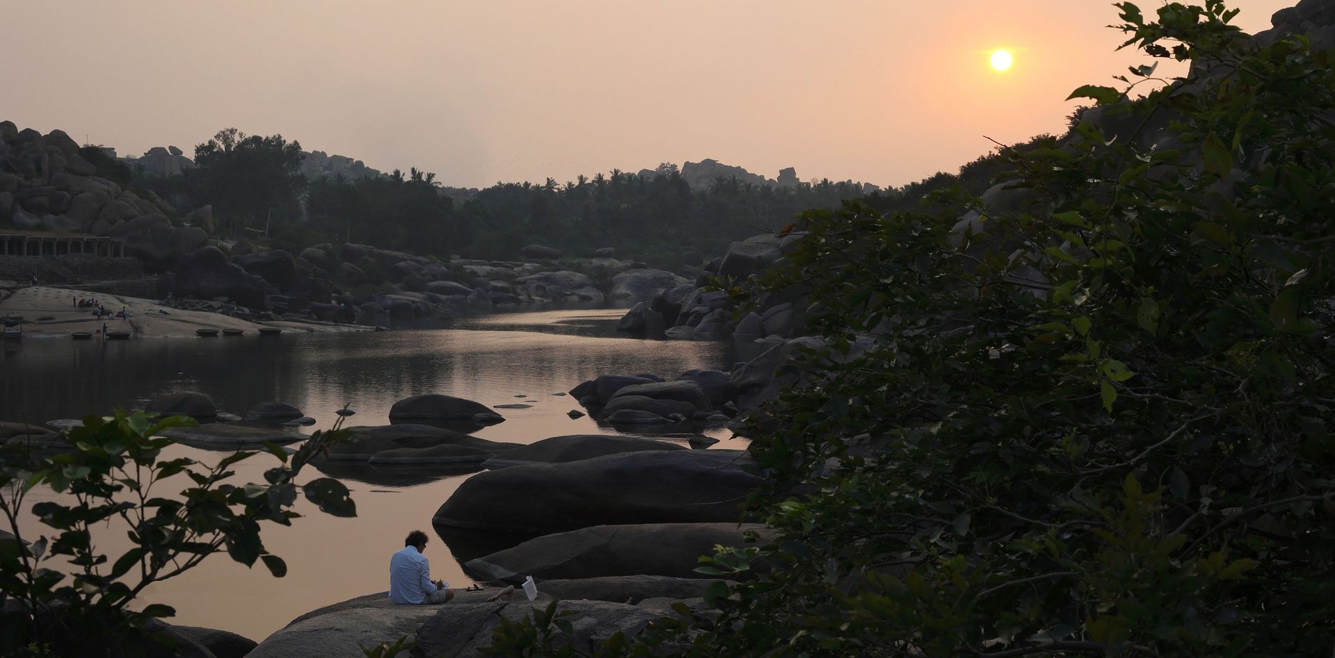 Sunset over Tungabhadra River with a person on rocks.