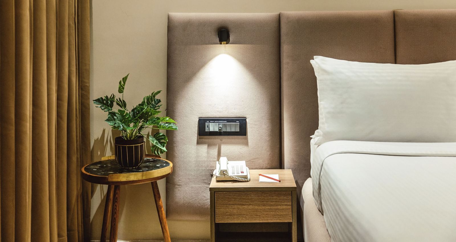 A close-up of a bed with a plant on a bedside table in a room at Mango Hill Central, Chennai.