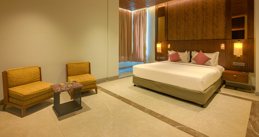 Spacious hotel bedroom with a king size bed, wooden ceiling, upholstered seating, bedside lighting and a large television.