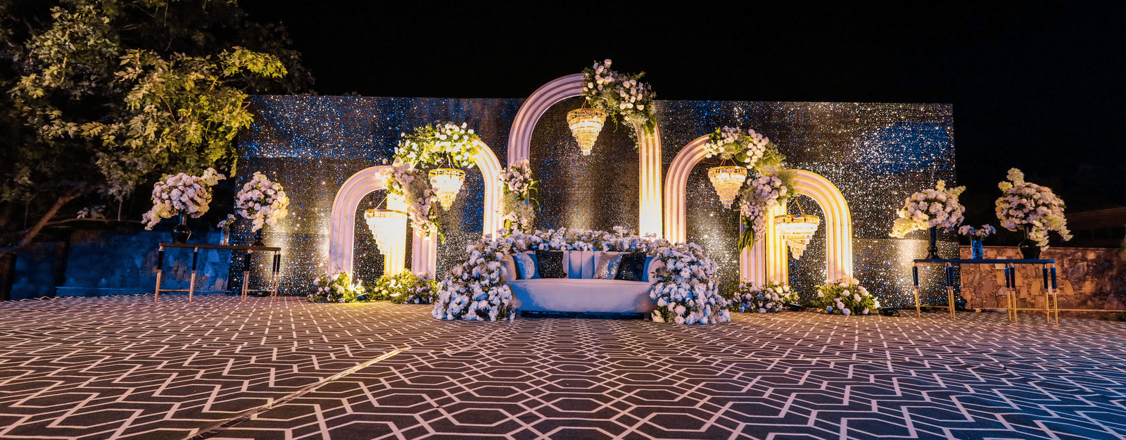 Grand outdoor wedding stage with geometric floor at Ananta Spa & Resort, Jaipur, featuring floral arches at night.