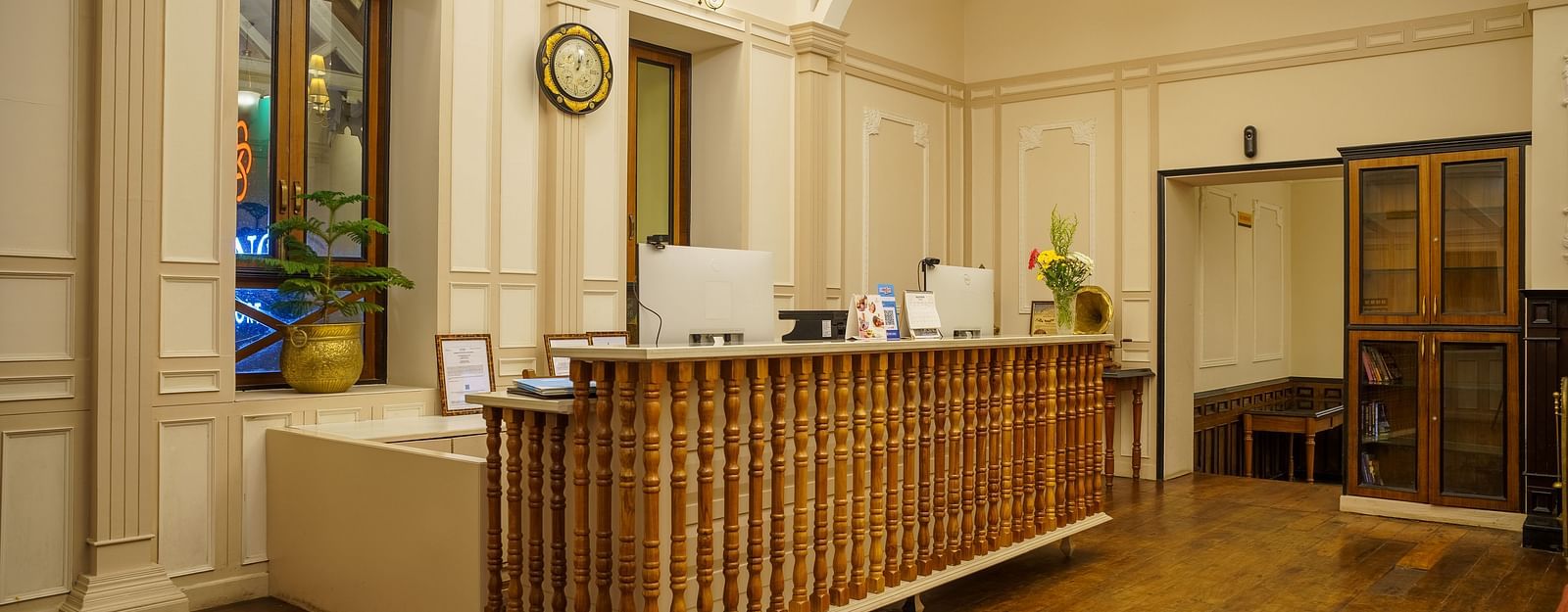 A reception desk at Orsino Spa Resort is made of light-coloured wood in a spacious room with ornate ceilings and chandeliers.