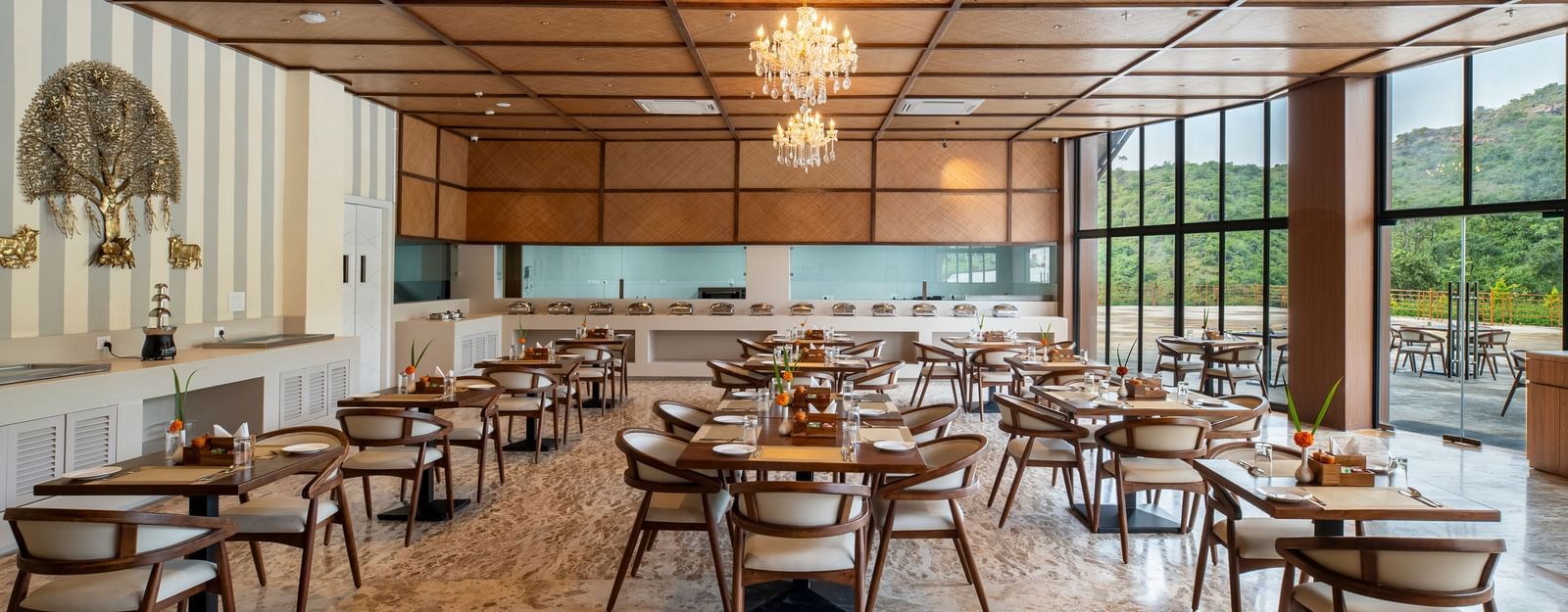 A well-lit restaurant interior at Osian Valley Resort & Spa with multiple square wooden tables and chairs arranged on a patterned floor. 