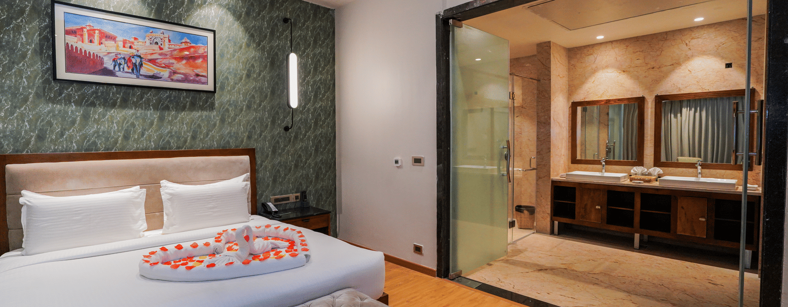 A room with a bed decorated with petals and an attached glass-walled bathroom at Pushkara Resort & Spa.