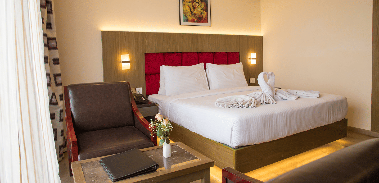 Side angle view of a double bed in a brightly lit Deluxe Room with a back lit headboard at the Benzz Park, Vellore.