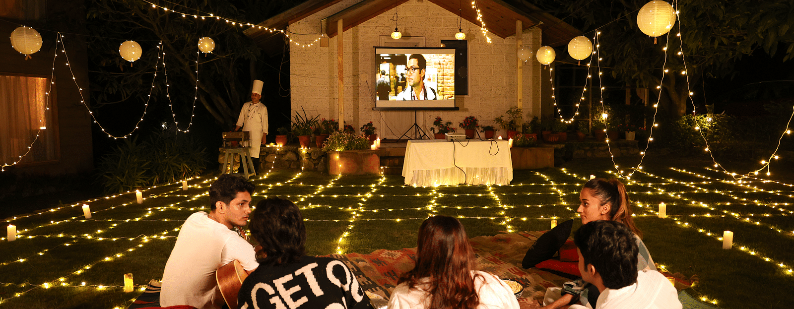 People enjoying an open movie night setup with lights and a projector set up at The Sylvan Retreat, Dehradun. 