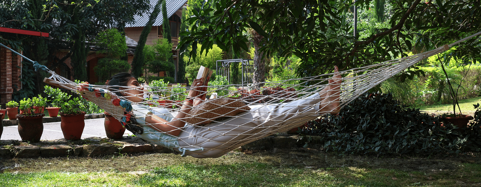 A woman laying on a hammock reading a book at A man flying a kite at The Sylvan Retreat, Dehradun.