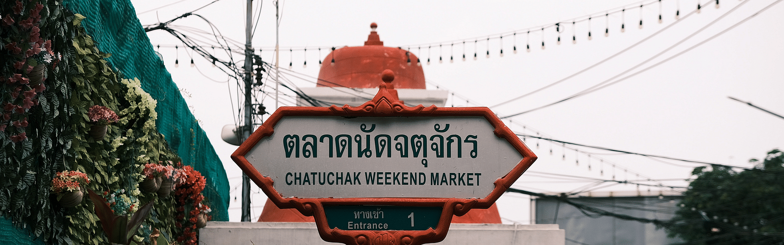 a signage of Chatuchak Weekend Market at the entrance of the event space with white clouds in the background
