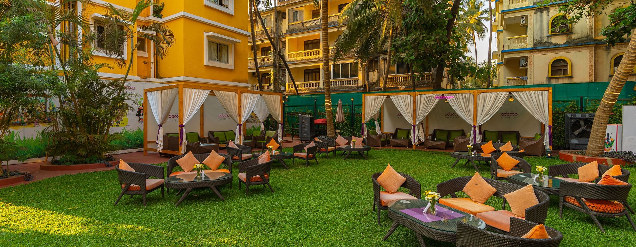 An image of a lawn area featuring seating arrangements, framed by vibrant yellow buildings.