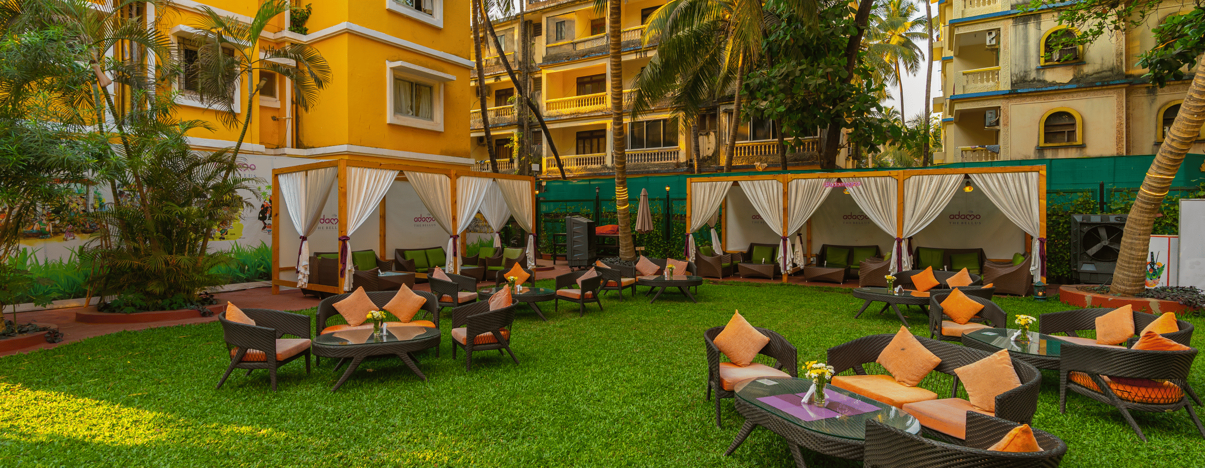 An image of a lawn area featuring seating arrangements, framed by vibrant yellow buildings.