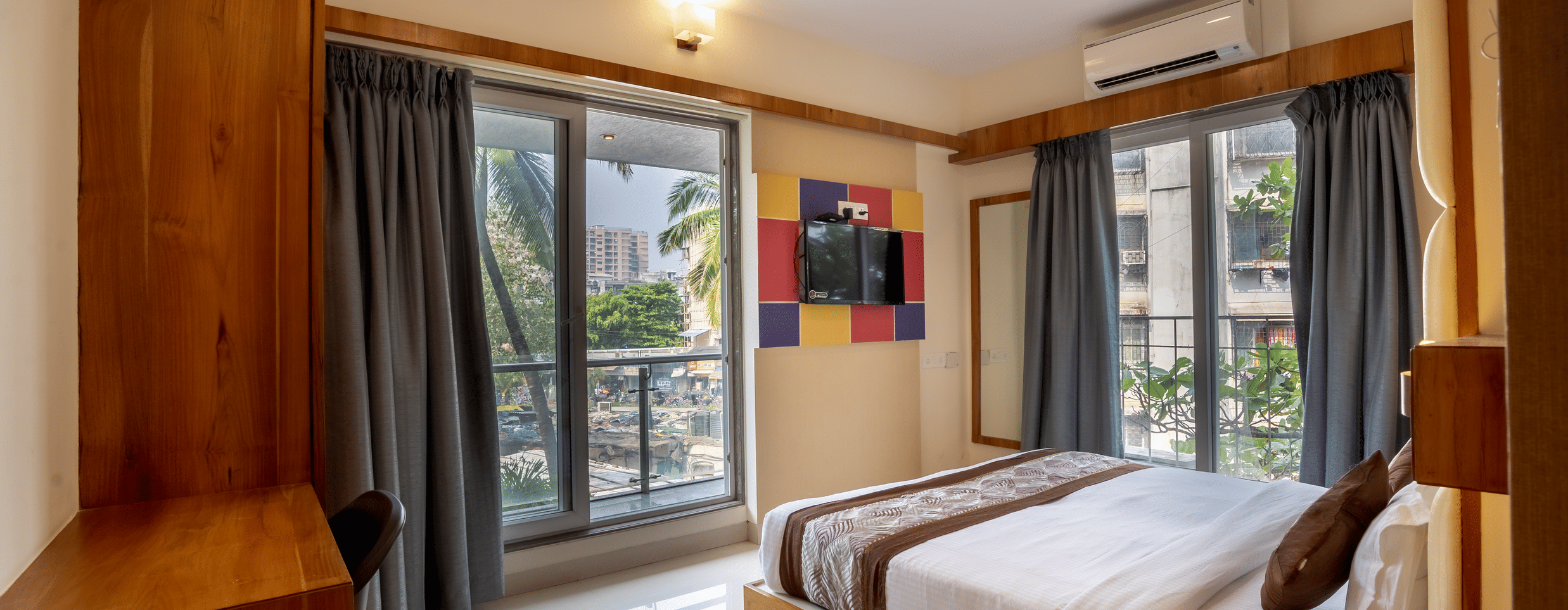 Home2 Suites & Service Apartments featuring a bed facing the TV on the wall with the door to balcony next to it, ready to be booked with exciting offers at Home2 India available on the official website