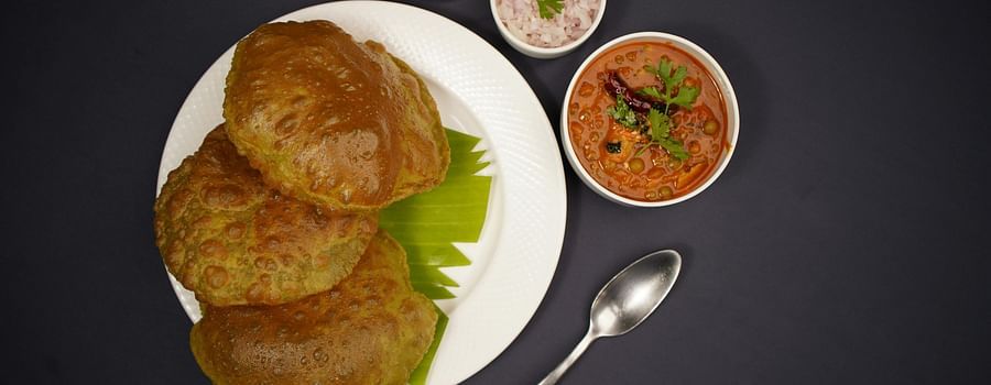 A plate of poori with channa, served with onions, lemon, and pickle.