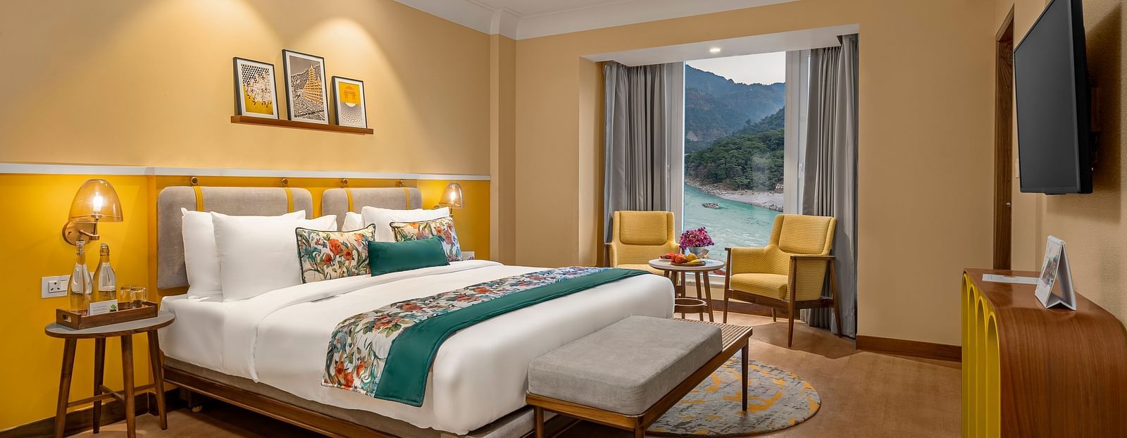  The room features a king-size bed with a plush headboard and comofrtable bedding. Armchairs by the window, offering a scenic view of the mountains. The room also includes a wooden desk, a television, and a ceiling fan. 