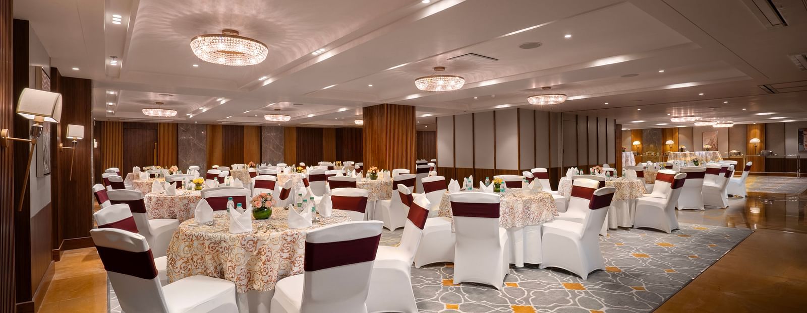 A spacious conference hall with round tables covered in tablecloths and chairs. and the room is decorated with chandeliers and wall lamps.