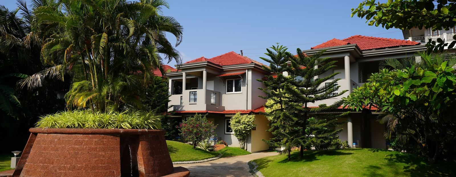 Facade of Argo By Trance, Goa with a red roof, surrounded by lush green trees and a well-maintained garden